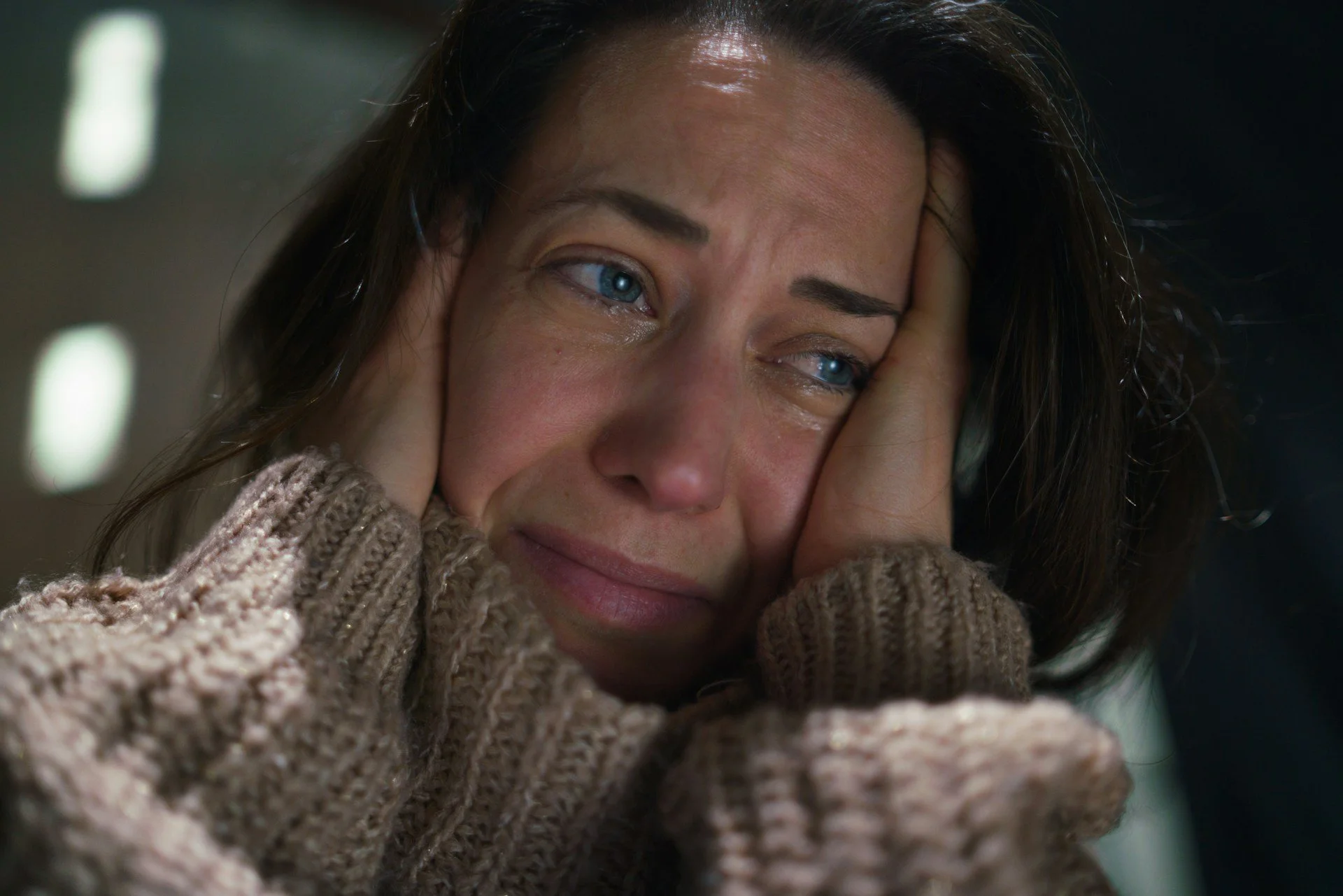 Middle-aged woman has hands on the sides of her head while crying.