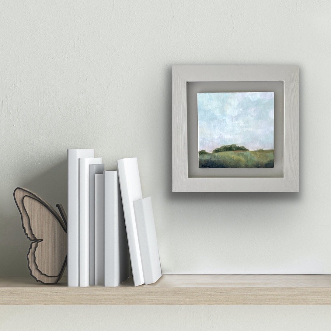 framed painting of a copse of trees on a hill hung on a wall