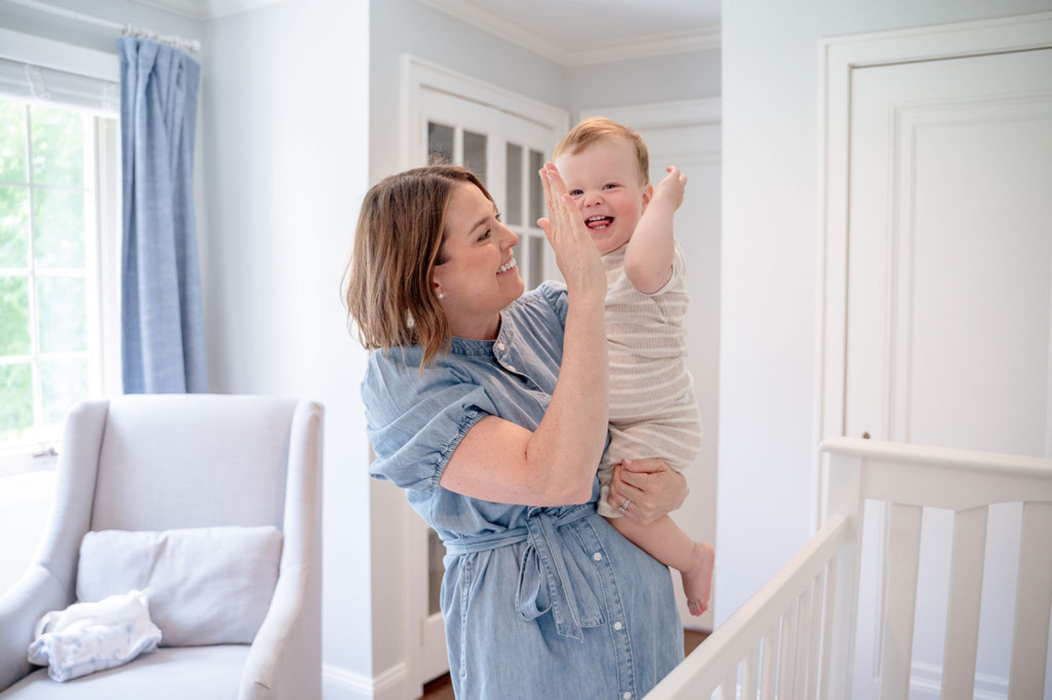 A mom and her baby high five in front of a crib.