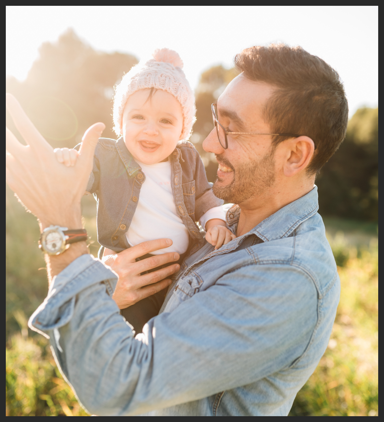 Backlit photo of dad high fiving with his baby in celebration in a grass field with