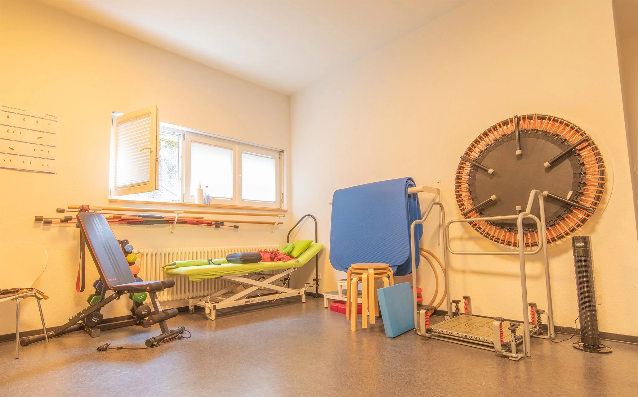 Fitnessraum mit Trainingsgeräten, Hantelbank, Gymnastikmatten, Therapie- und Sportgeräte, 3 Fenster, gelbe Wände.