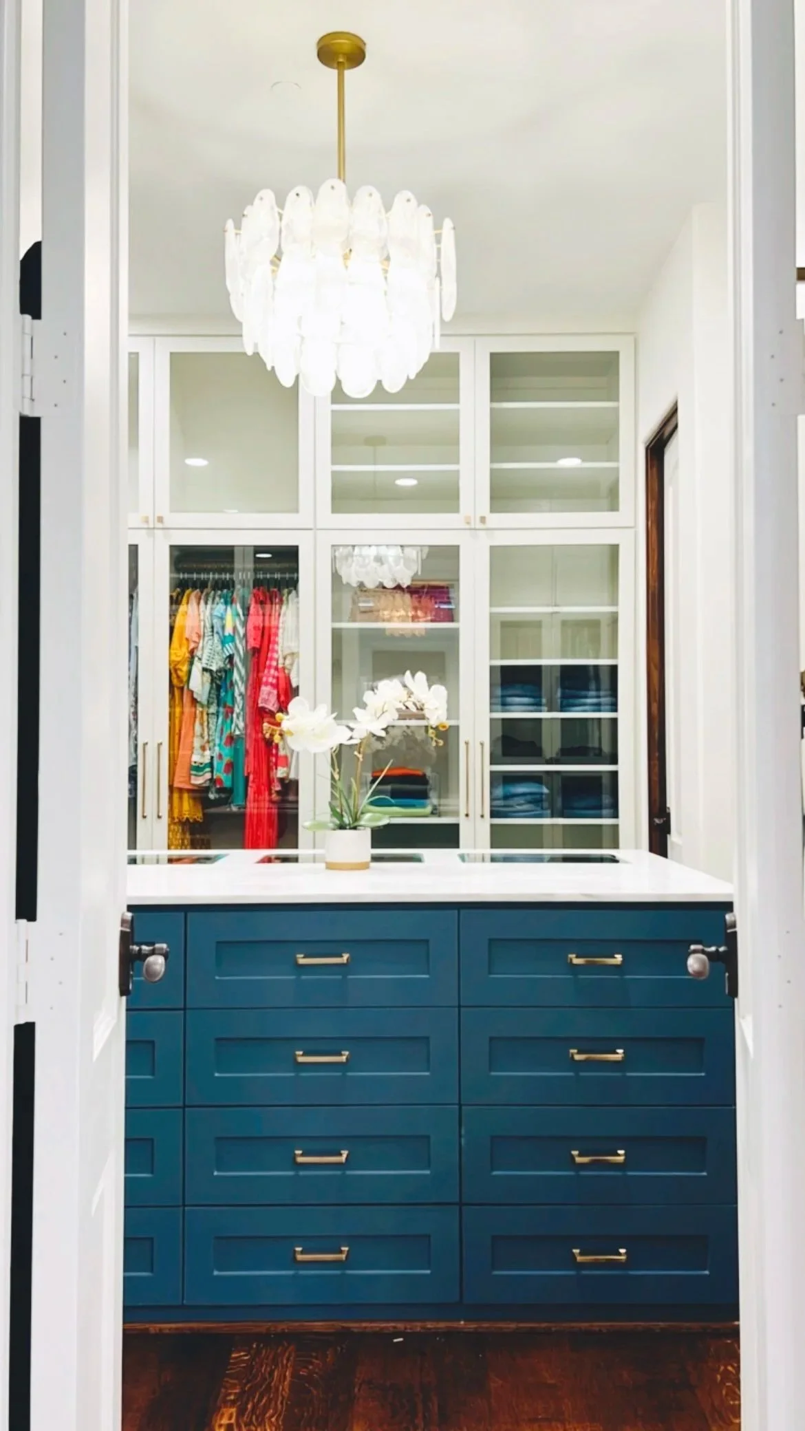 Elegant master suite walk-in closet with custom cream built-in storage, glass-front cabinetry, and a navy storage island with drawers, designed and organized for a Preston Hollow home in Dallas, Texas.