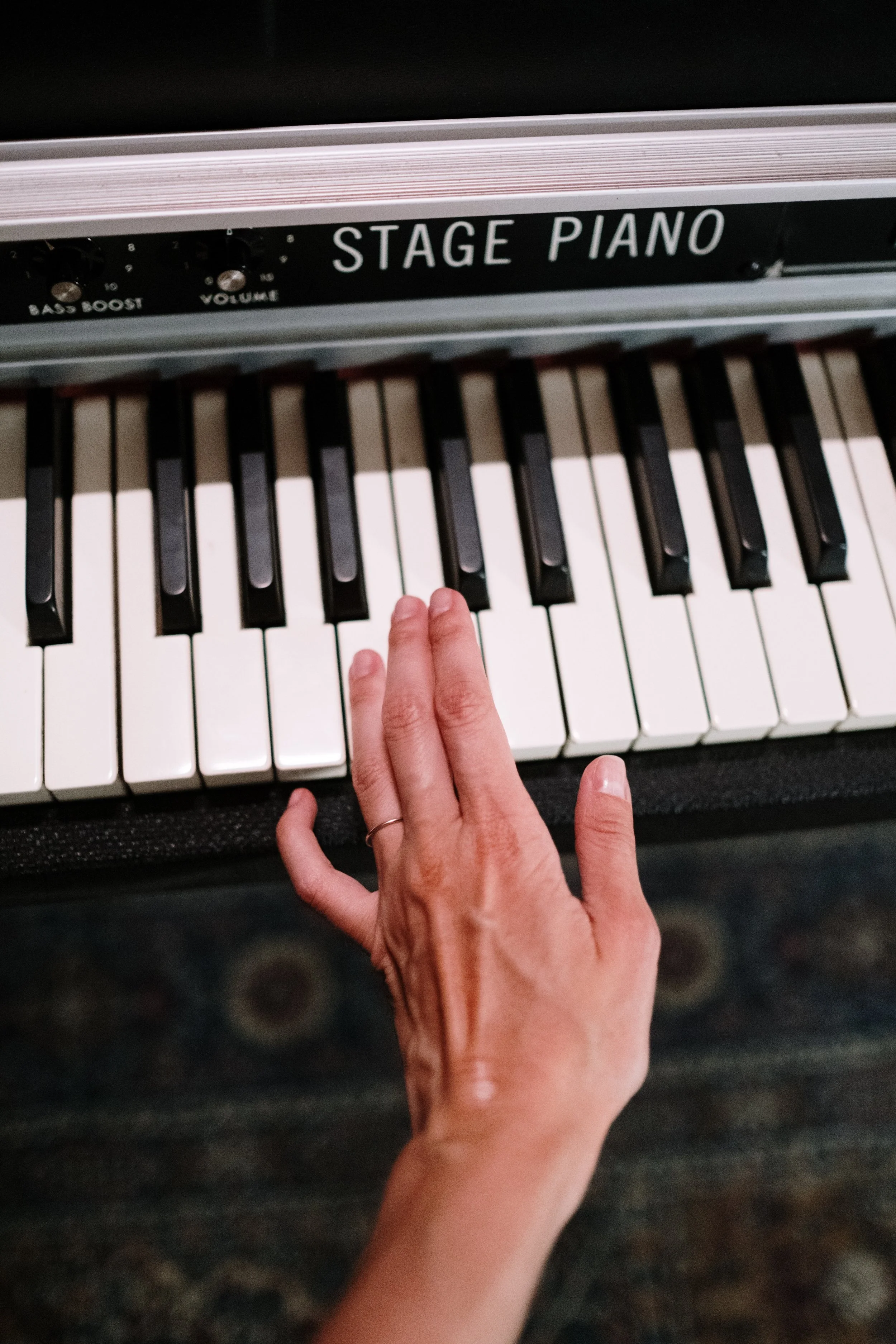A person playing piano, with a hand on the keys, labeled 'Stage Piano' with knobs for bass boost and volume.