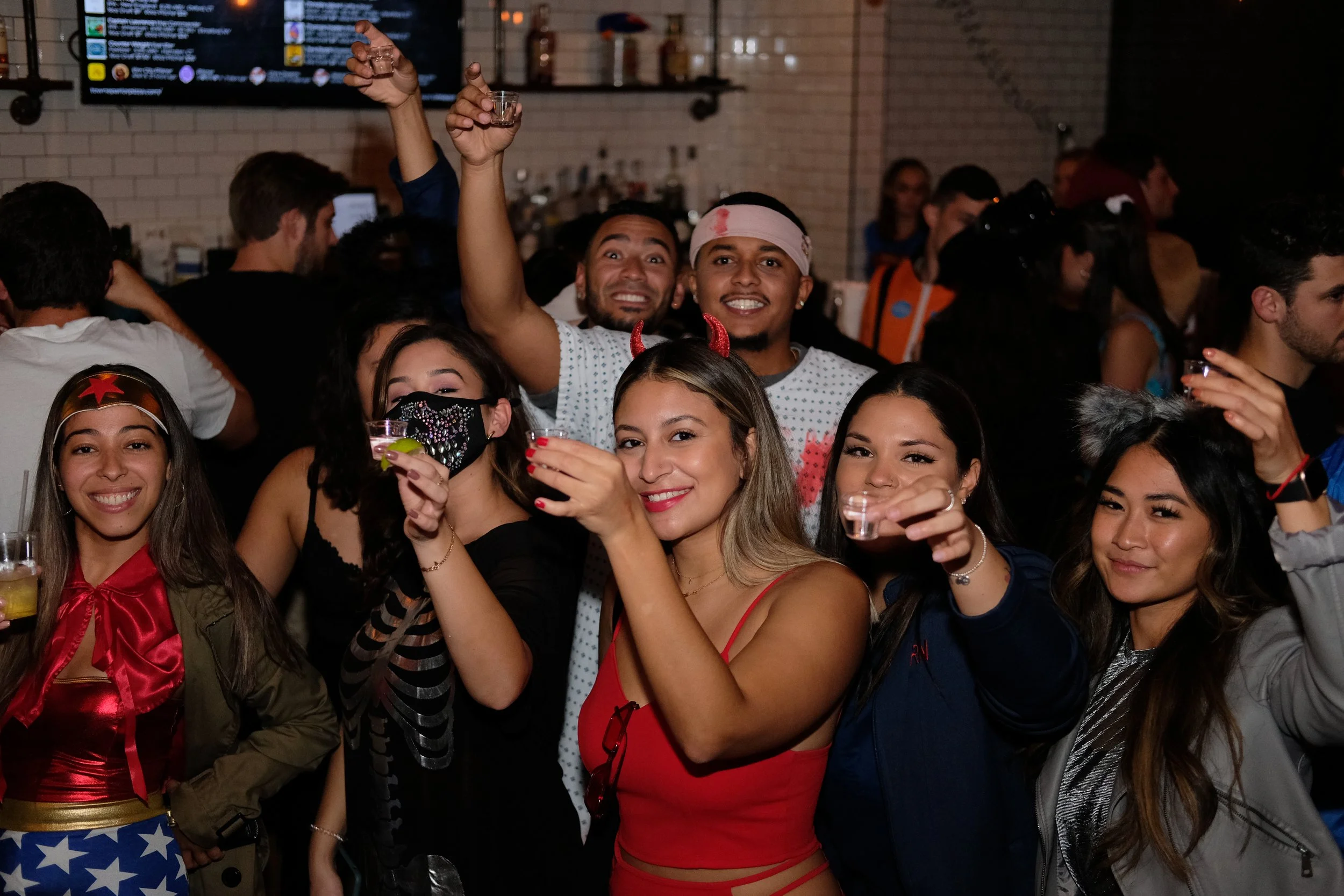 Group of people at a party wearing costumes, smiling and holding drinks.