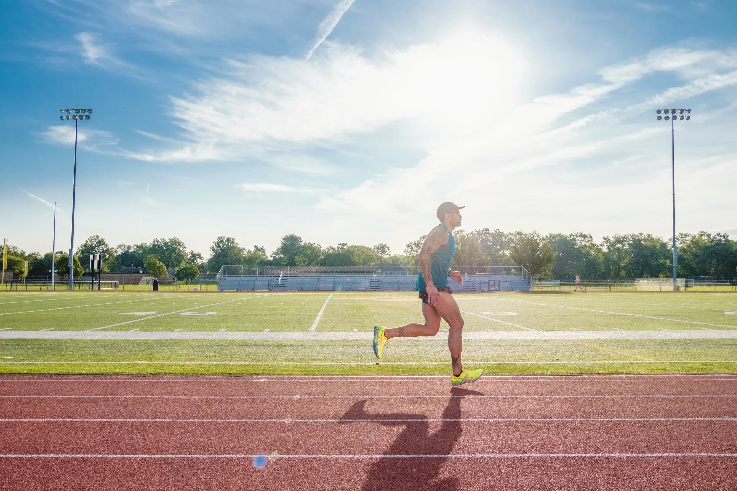 A person running on a track at a sports field on a sunny day with clear skies.