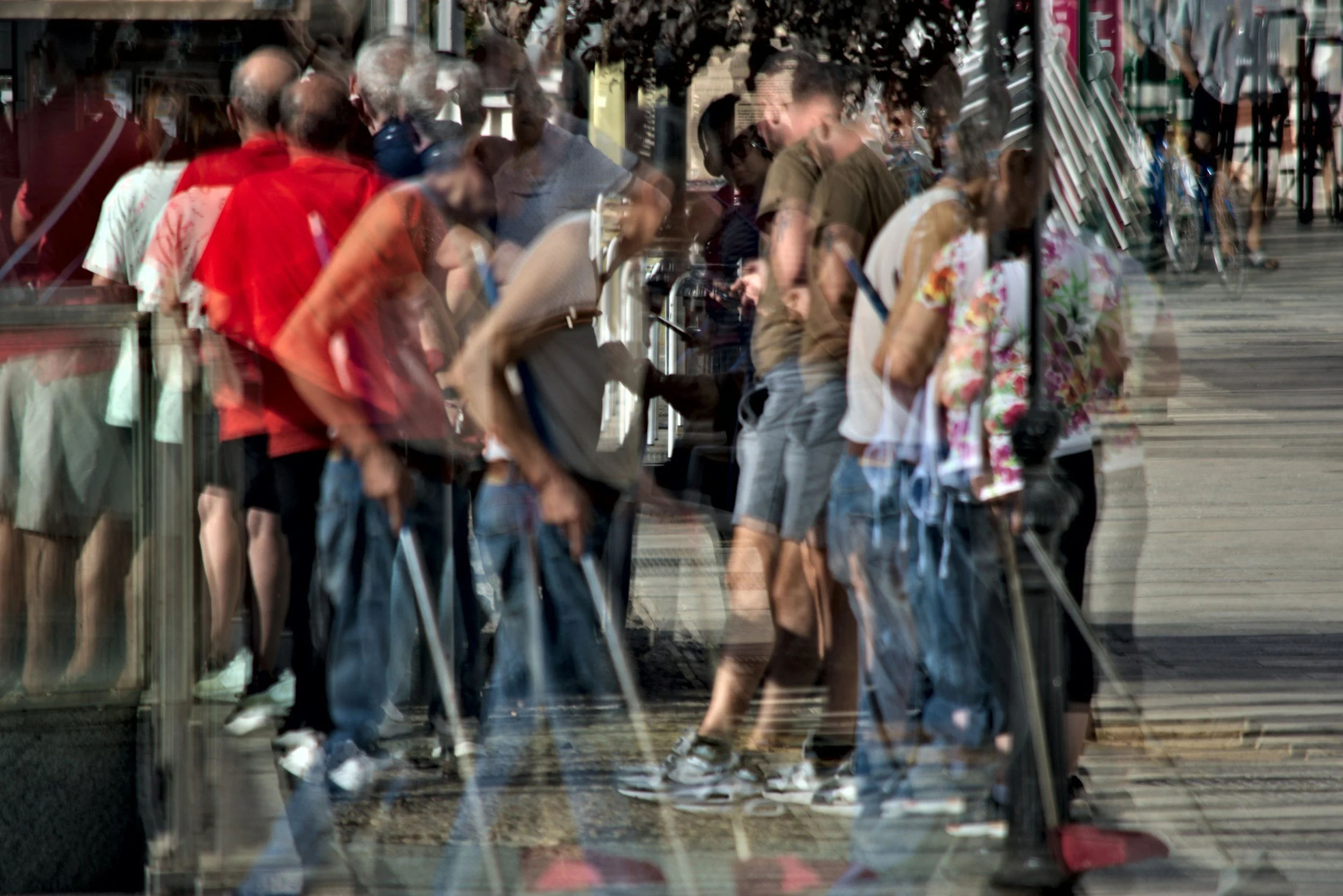 People walking in a line along a sidewalk seen through a glass window with reflections.