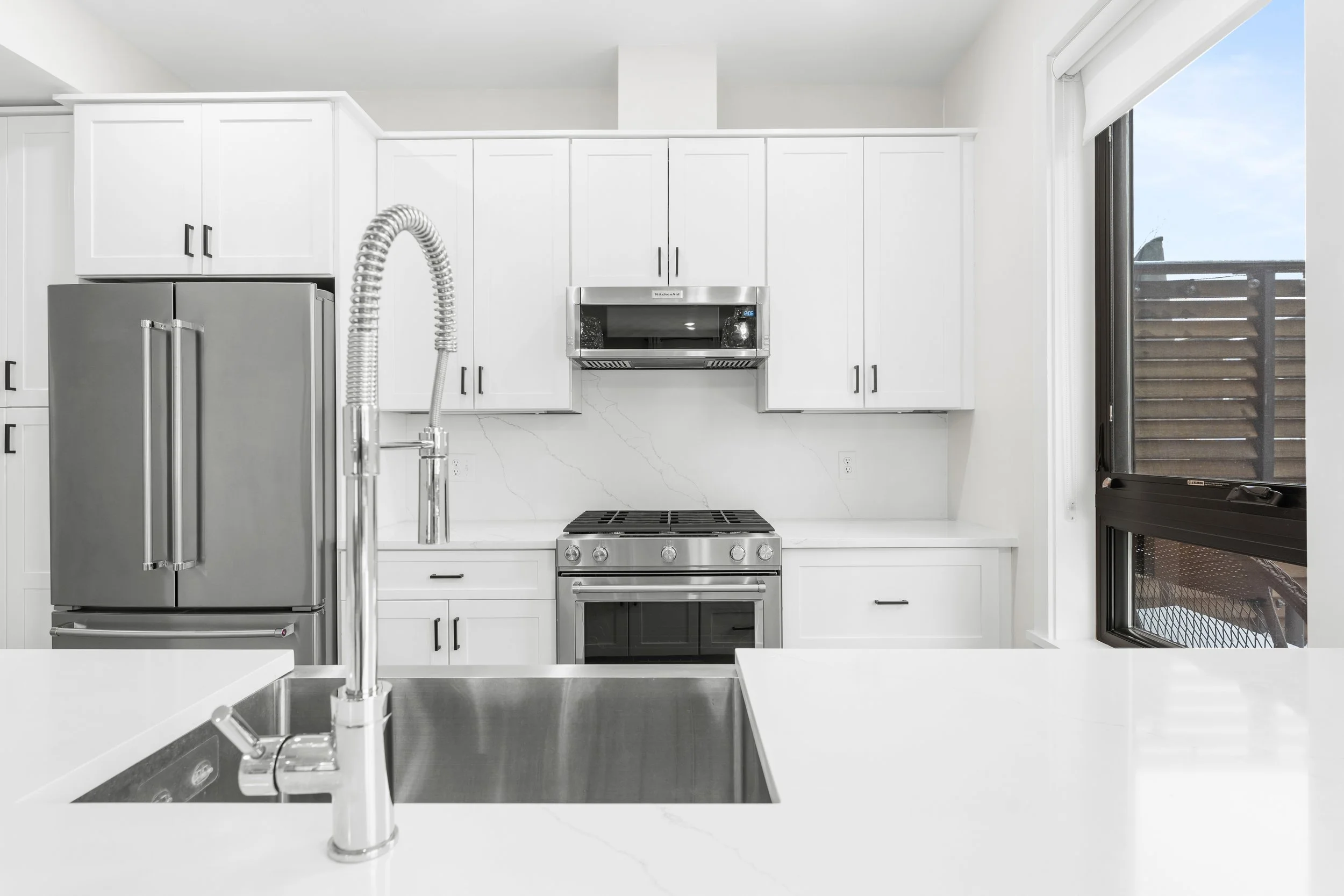 Modern kitchen with white cabinets, stainless steel appliances, a window, and a sink with a gooseneck faucet.