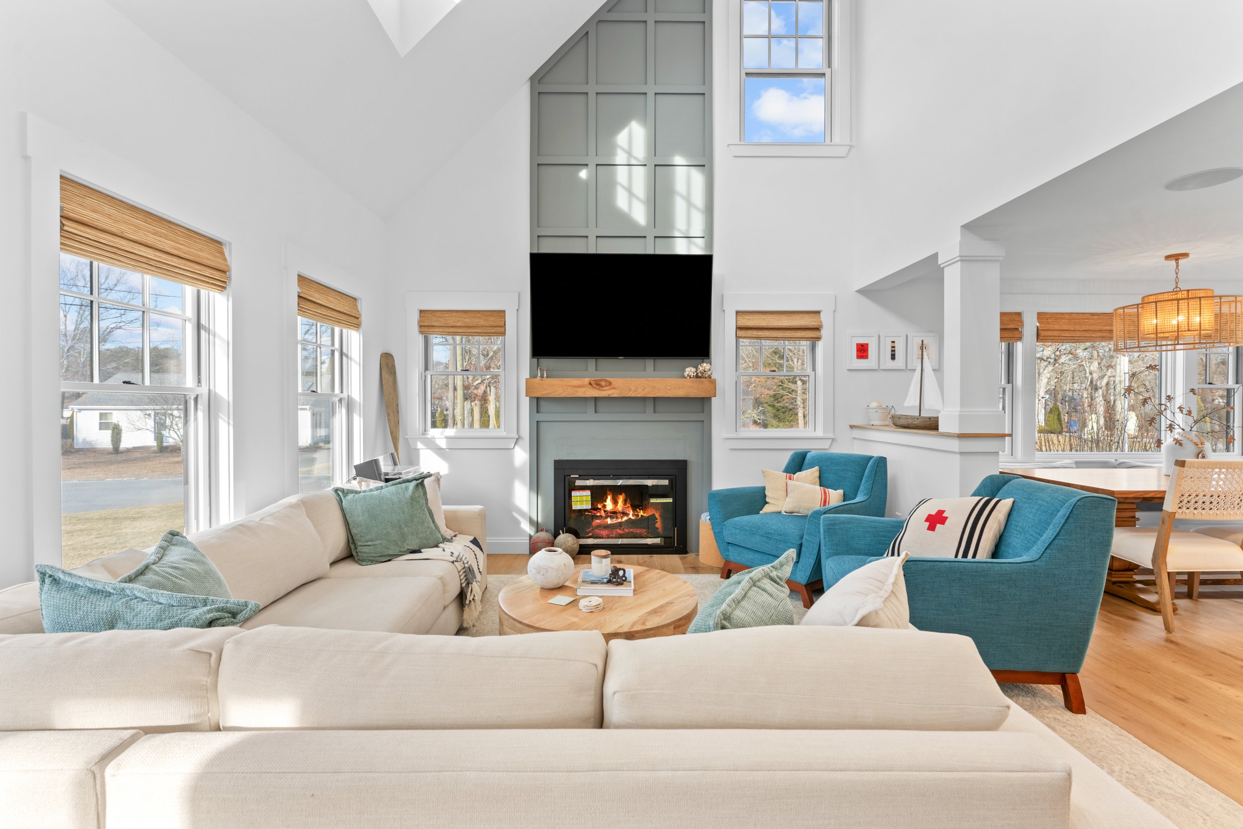 Bright living room with large windows, a fireplace, a beige sofa, blue armchairs, and wooden accents.