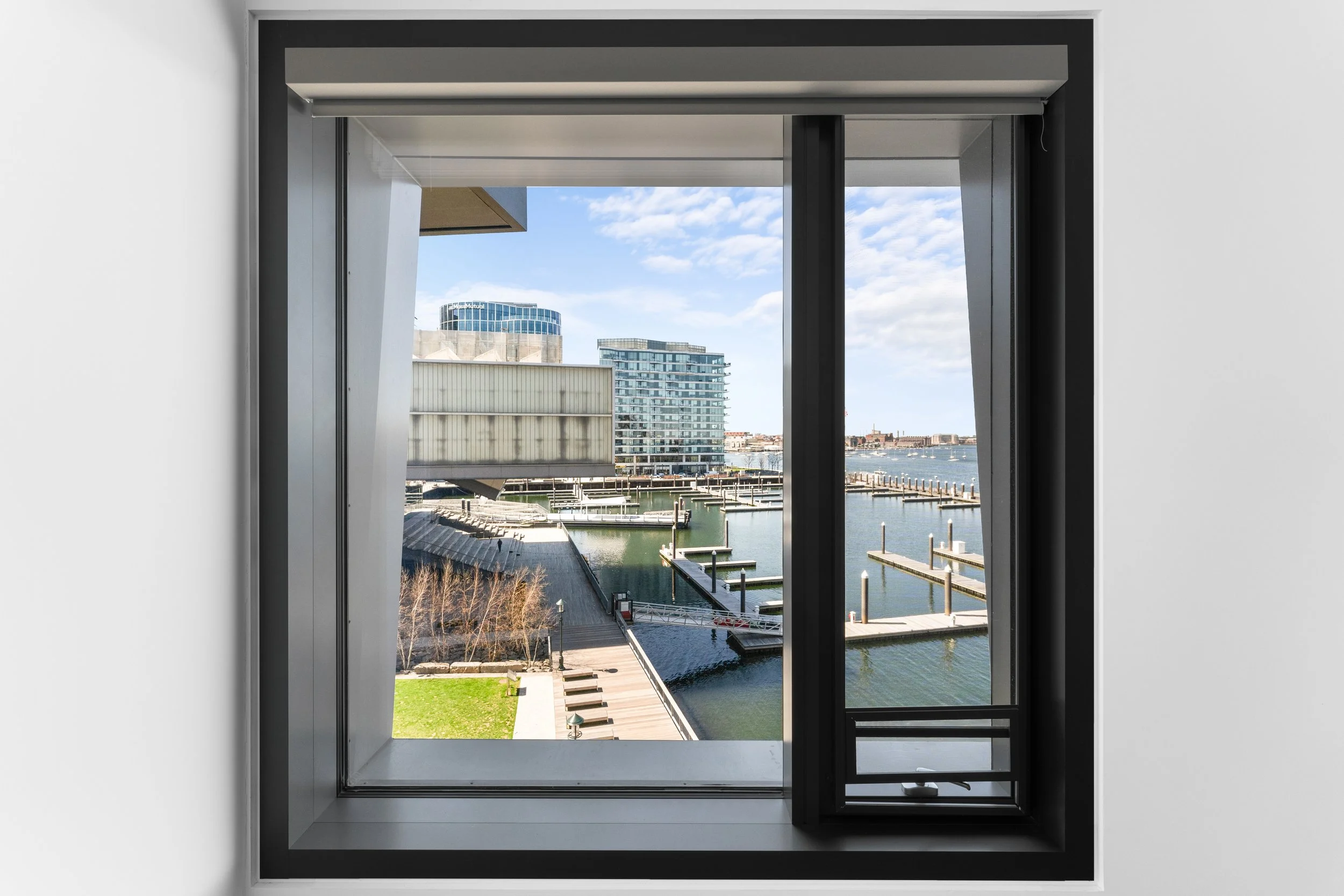 View of a cityscape and waterfront seen through a large modern window with black framing.