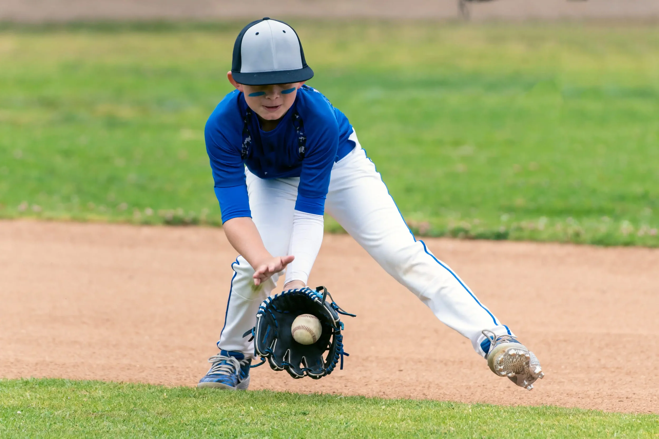 Baeball player in little league uniform fielding a ball.