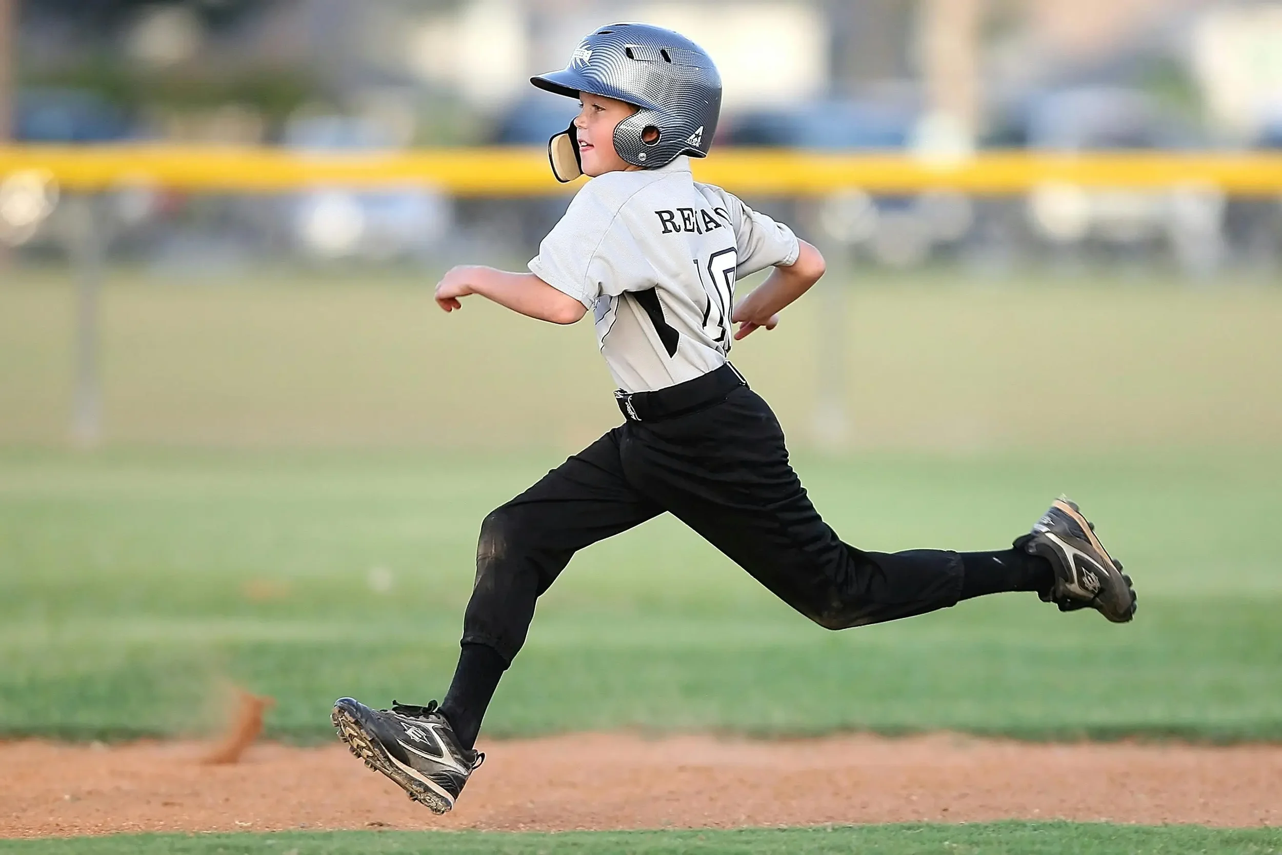 Little league player in uniform running the bases.