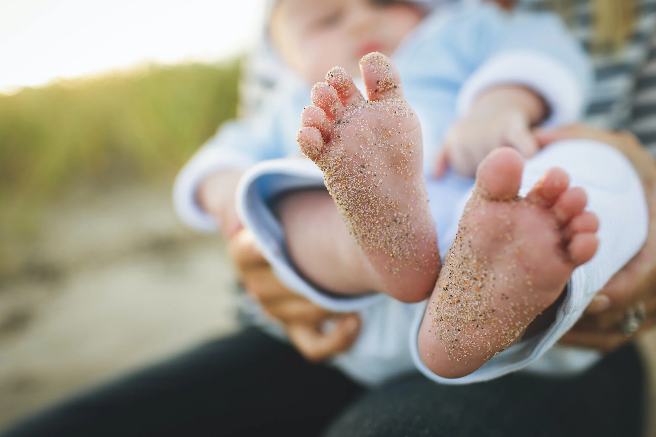 Close-up of a child's hand covered in colorful sand, with a blurred background of the child's face and outdoor setting.