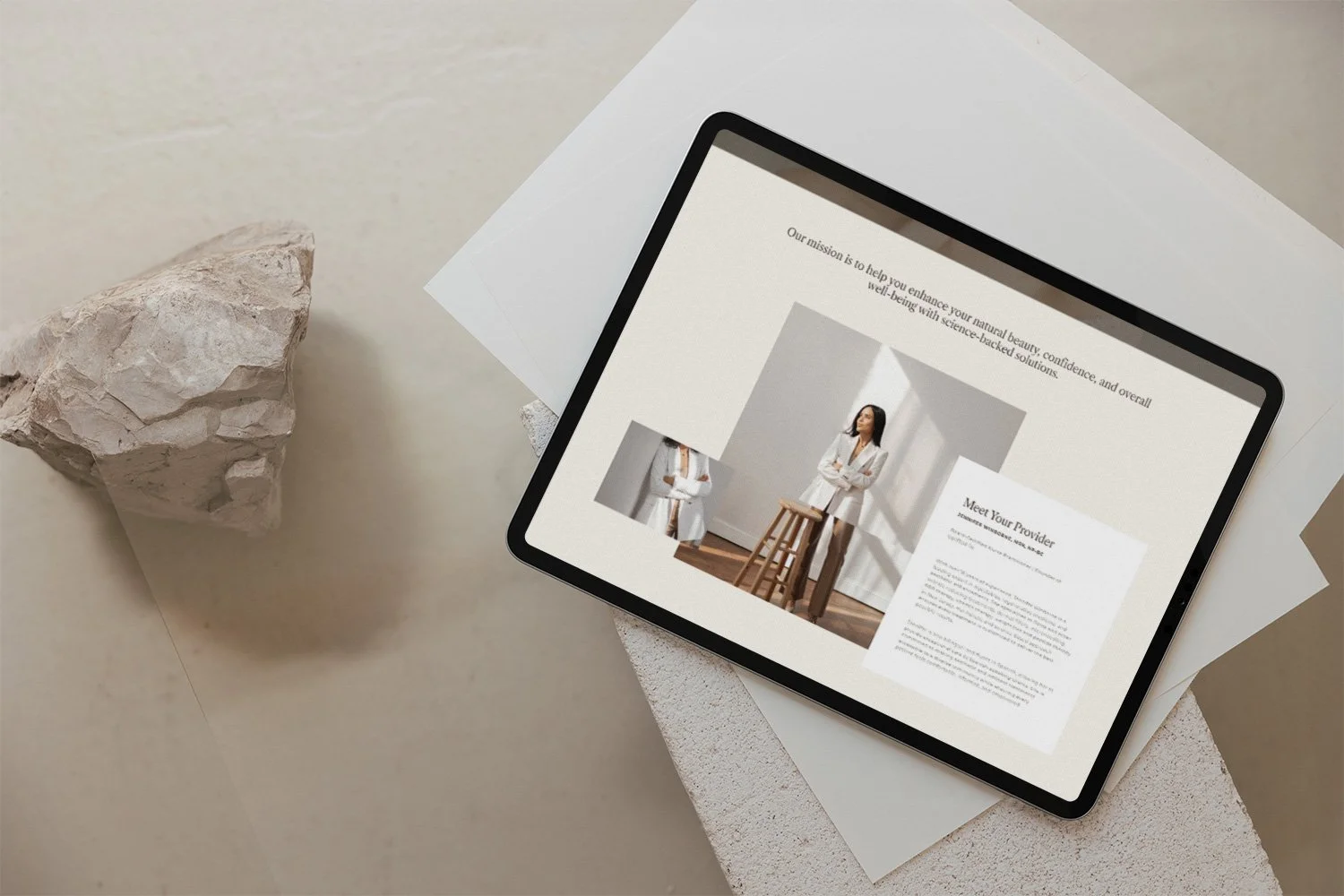 An iPad displaying a website with women in white coats, placed on a white surface with a chunk of stone nearby.