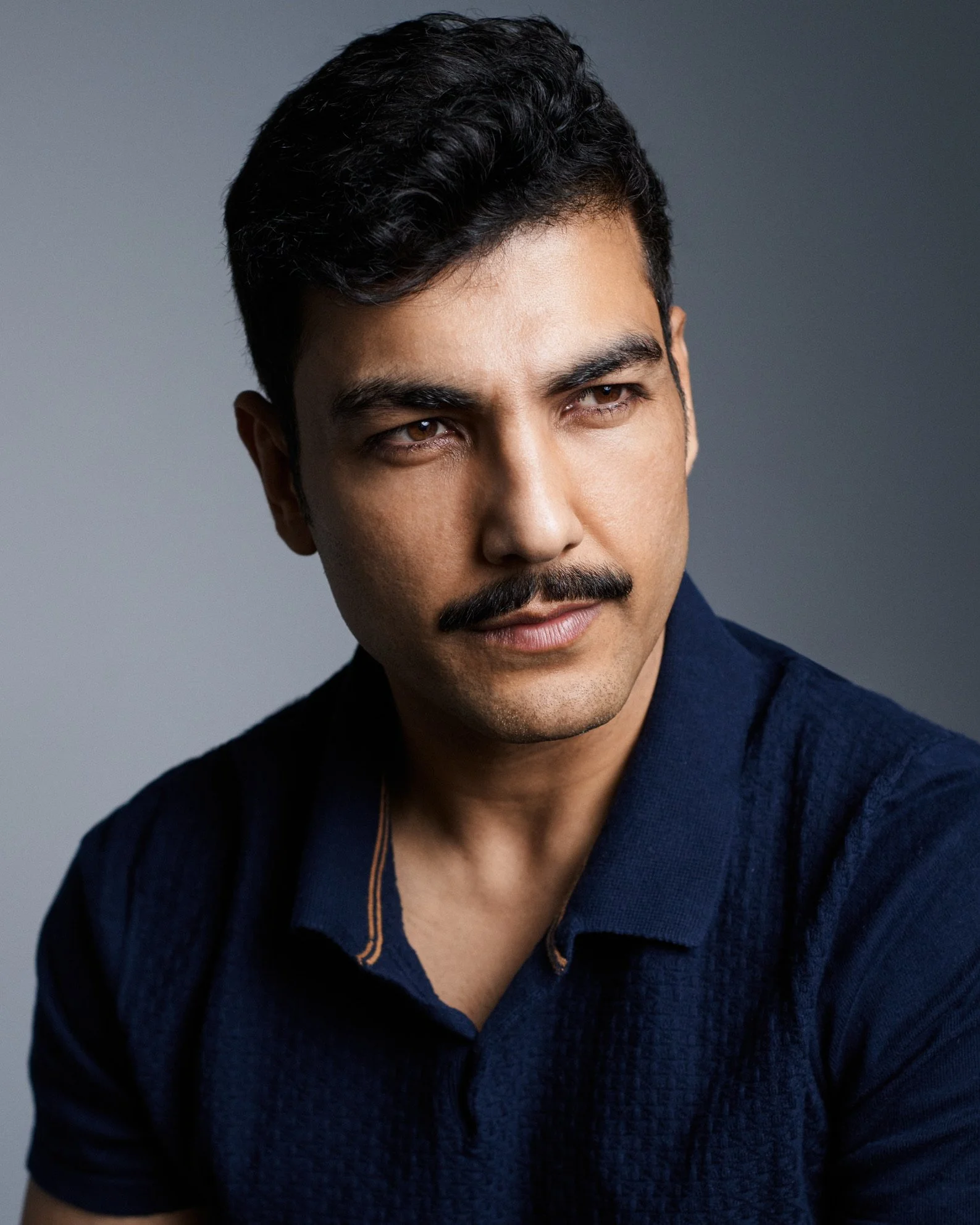 An Indian man in his forties with black hair and a black moustache wearing a dark blue shirt.
