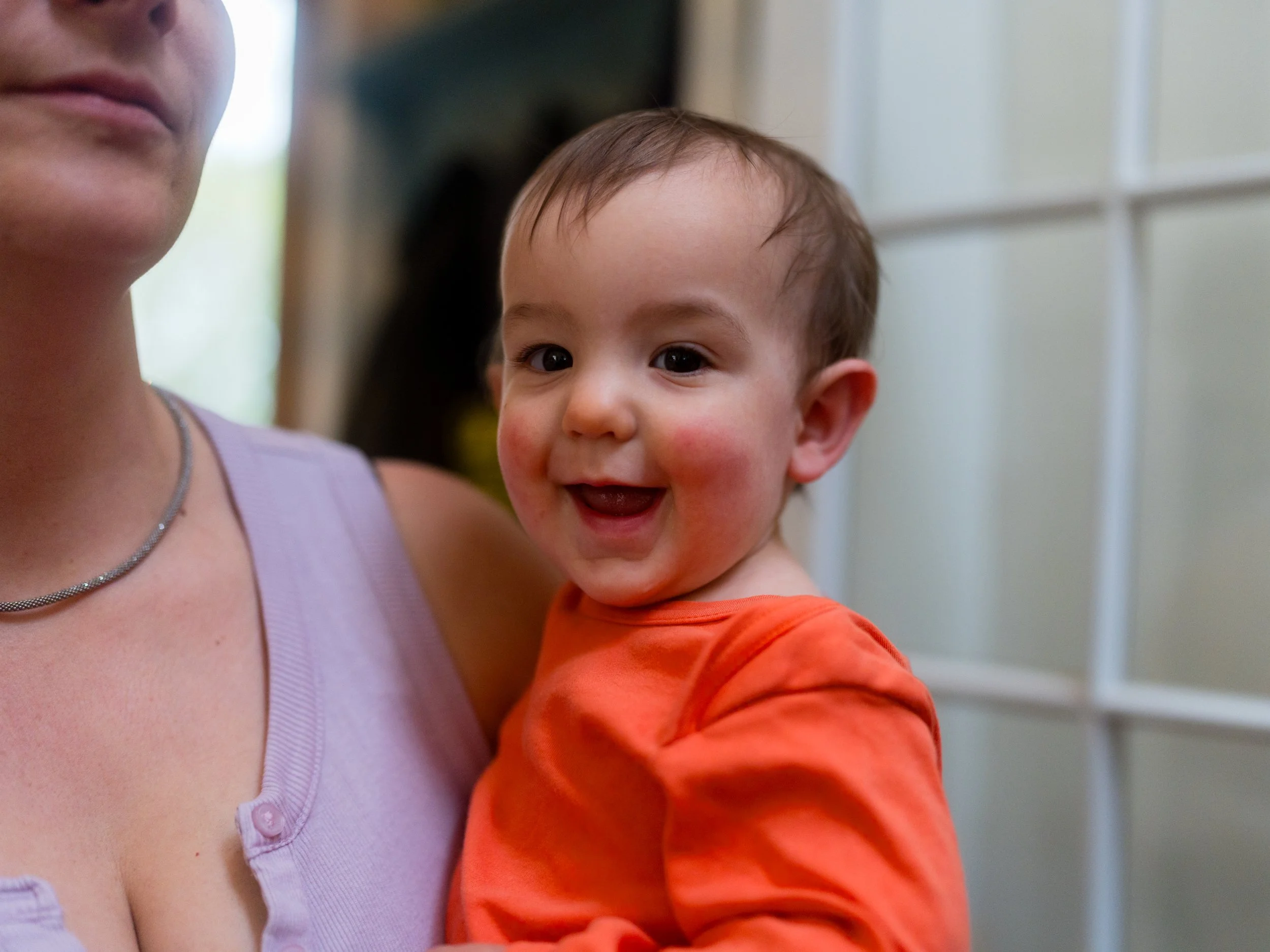 A baby with dark hair and rosy red cheeks smiling at the camera