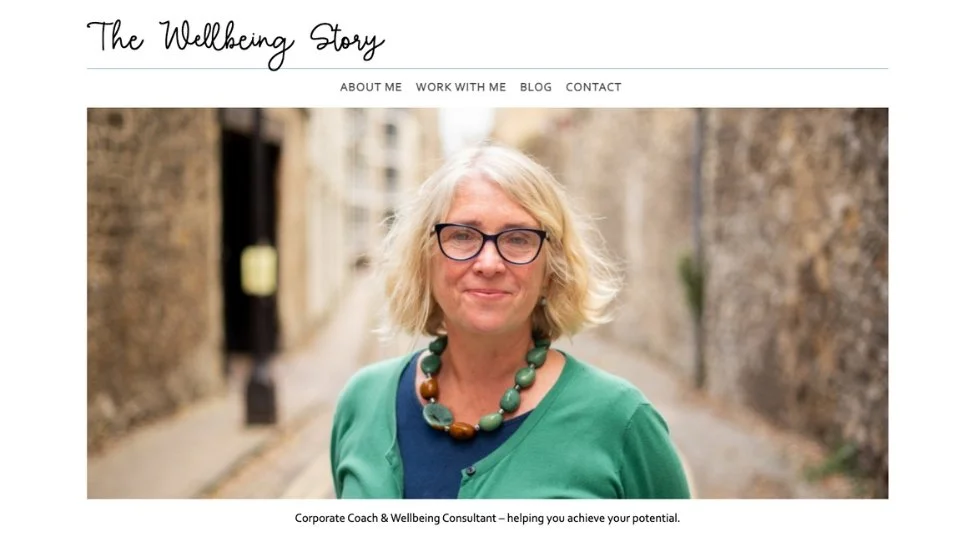 A smiling woman with glasses stands outside on a cobblestone path, showcasing web design on a wellbeing consultant’s homepage.