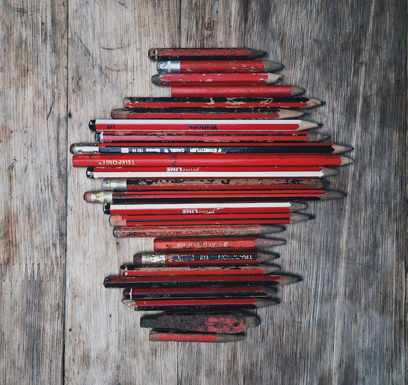 A collection of worn red and black pencils arranged vertically to resemble a human brain on a wooden surface.