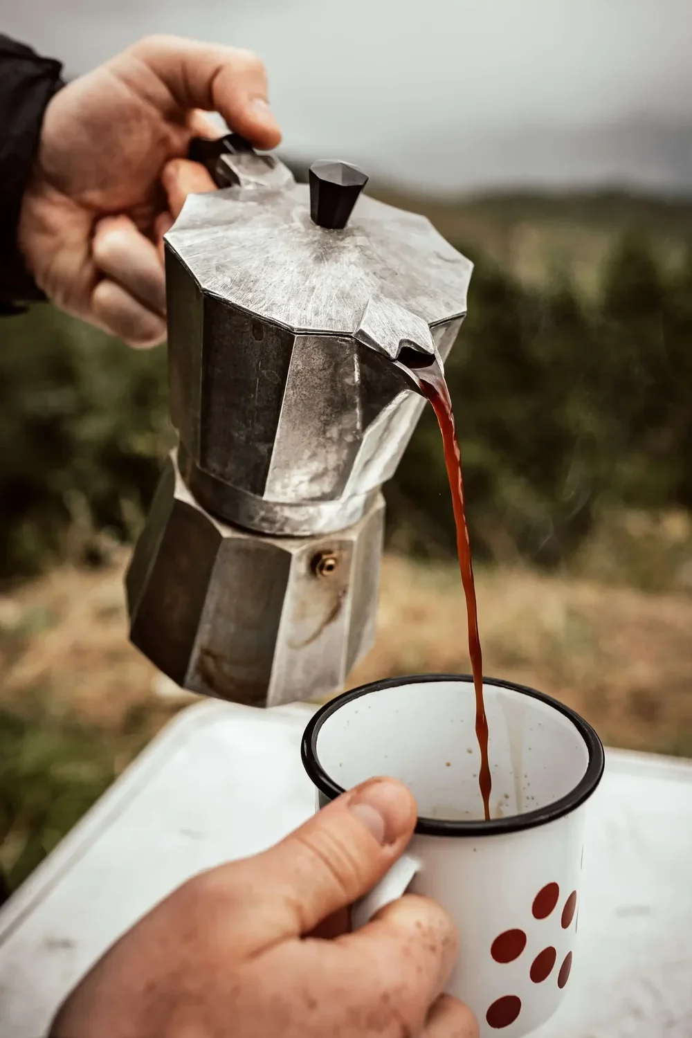 Moka pot pouring coffee into camping mug