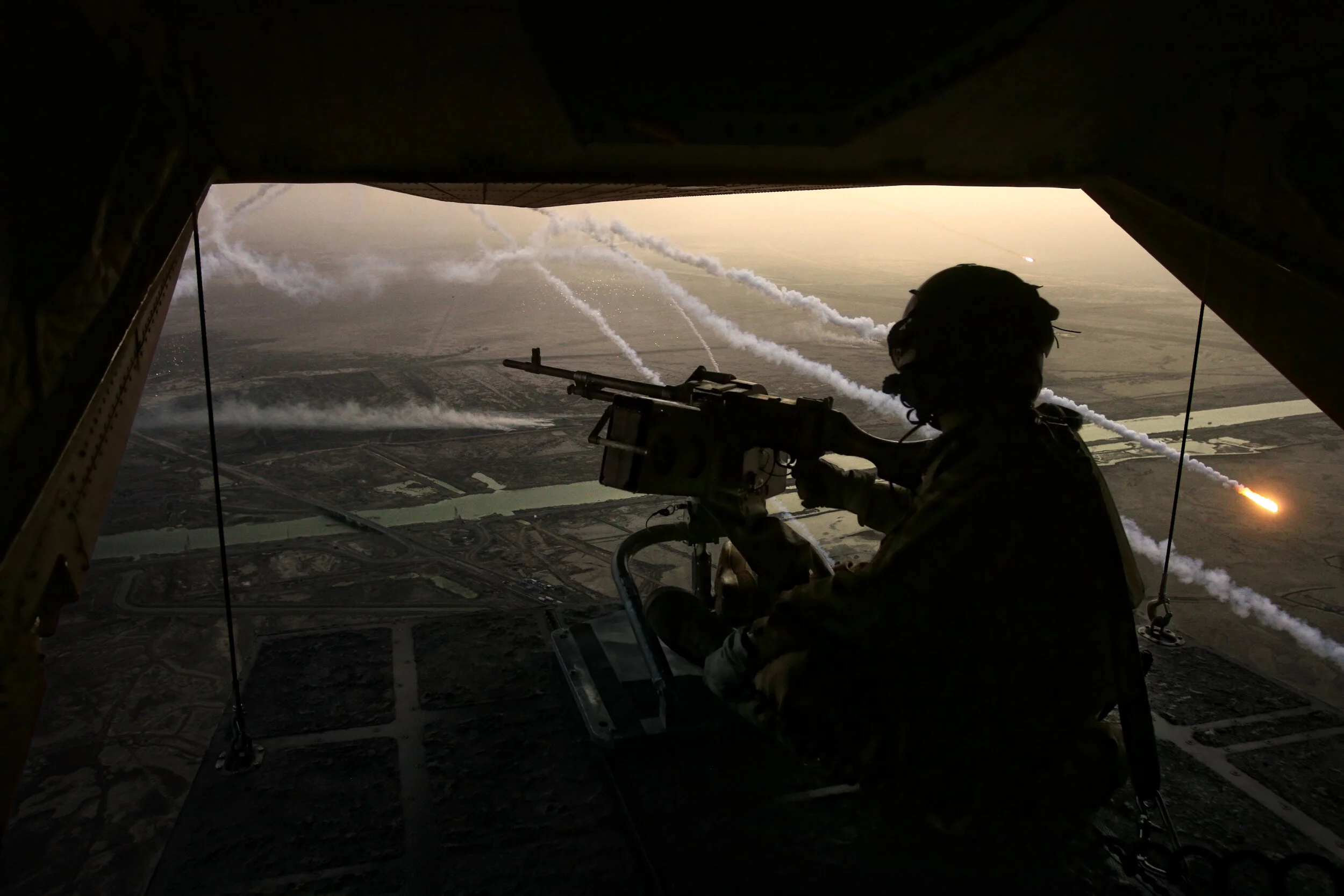 Famous Photograph by Lewis Whyld taken from inside a military aircraft. It shows a British rear gunner on the last combat operation of the war, as flares fire and the sun sets. Part of Whyld's war photography.