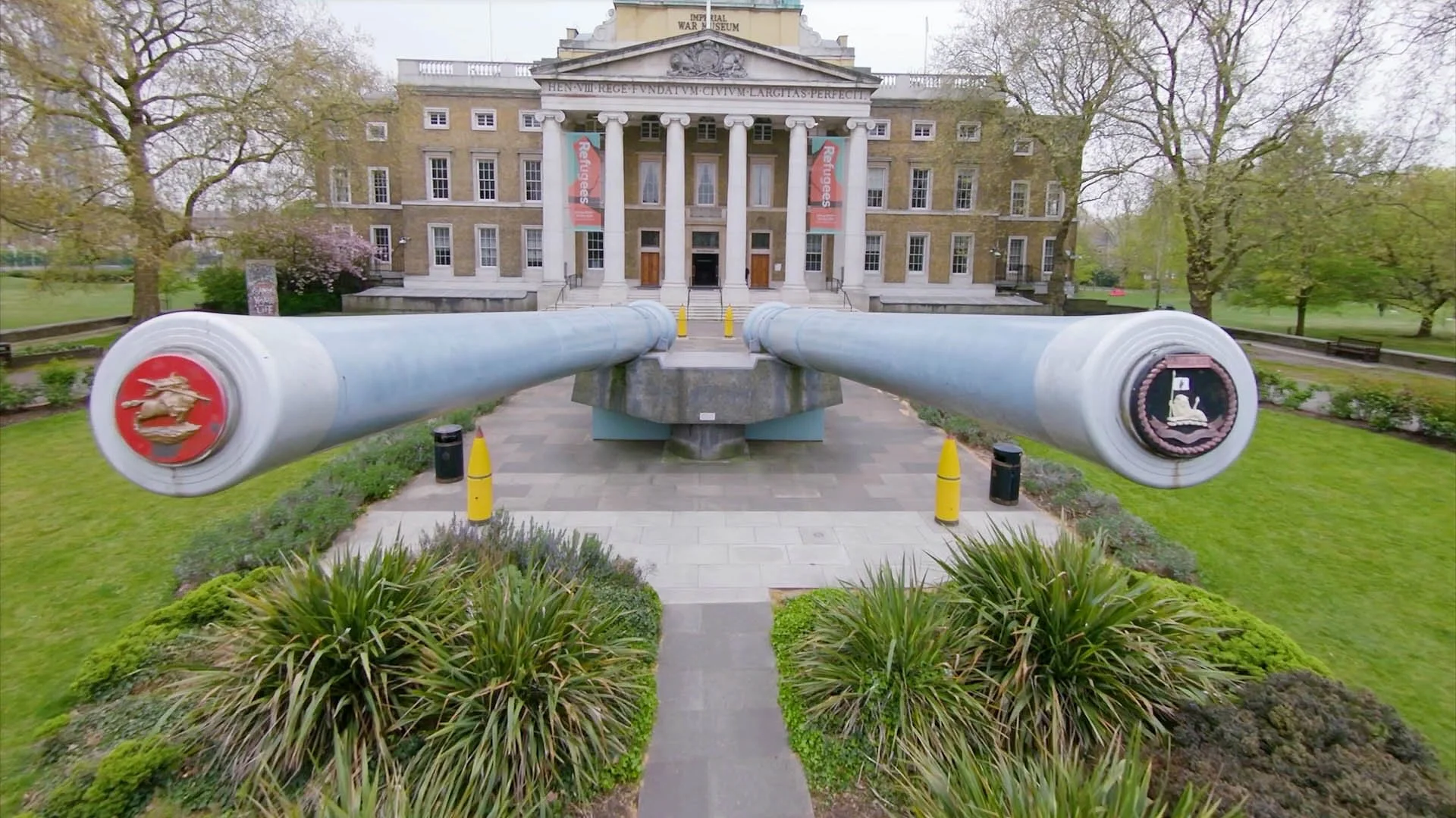 FPV drone view flying between historic artillery guns inside the Imperial War Museum London, showing the museum exhibits, gallery space and dramatic interior architecture.