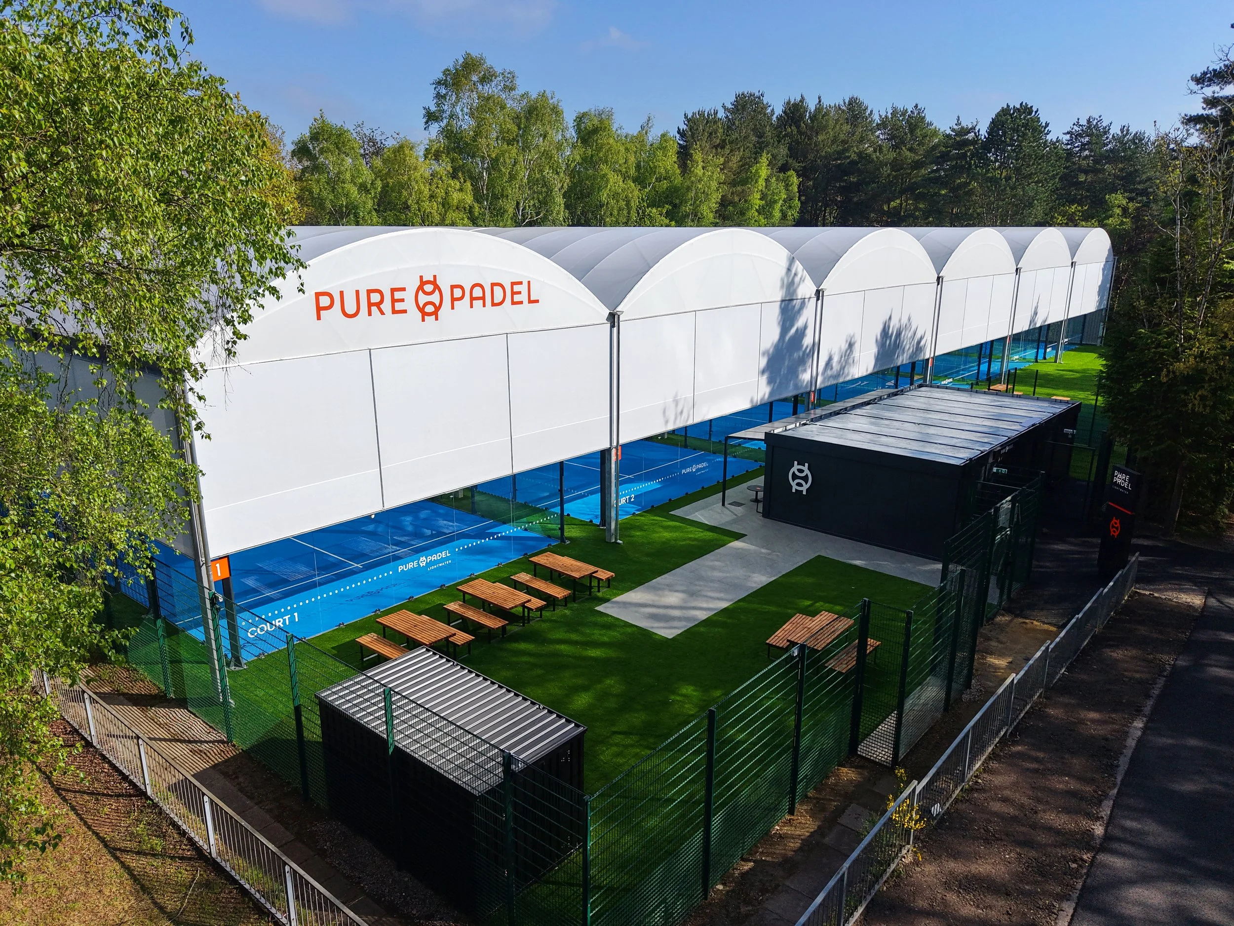 Aerial view of padel courts surrounded by woodland and sports fields.