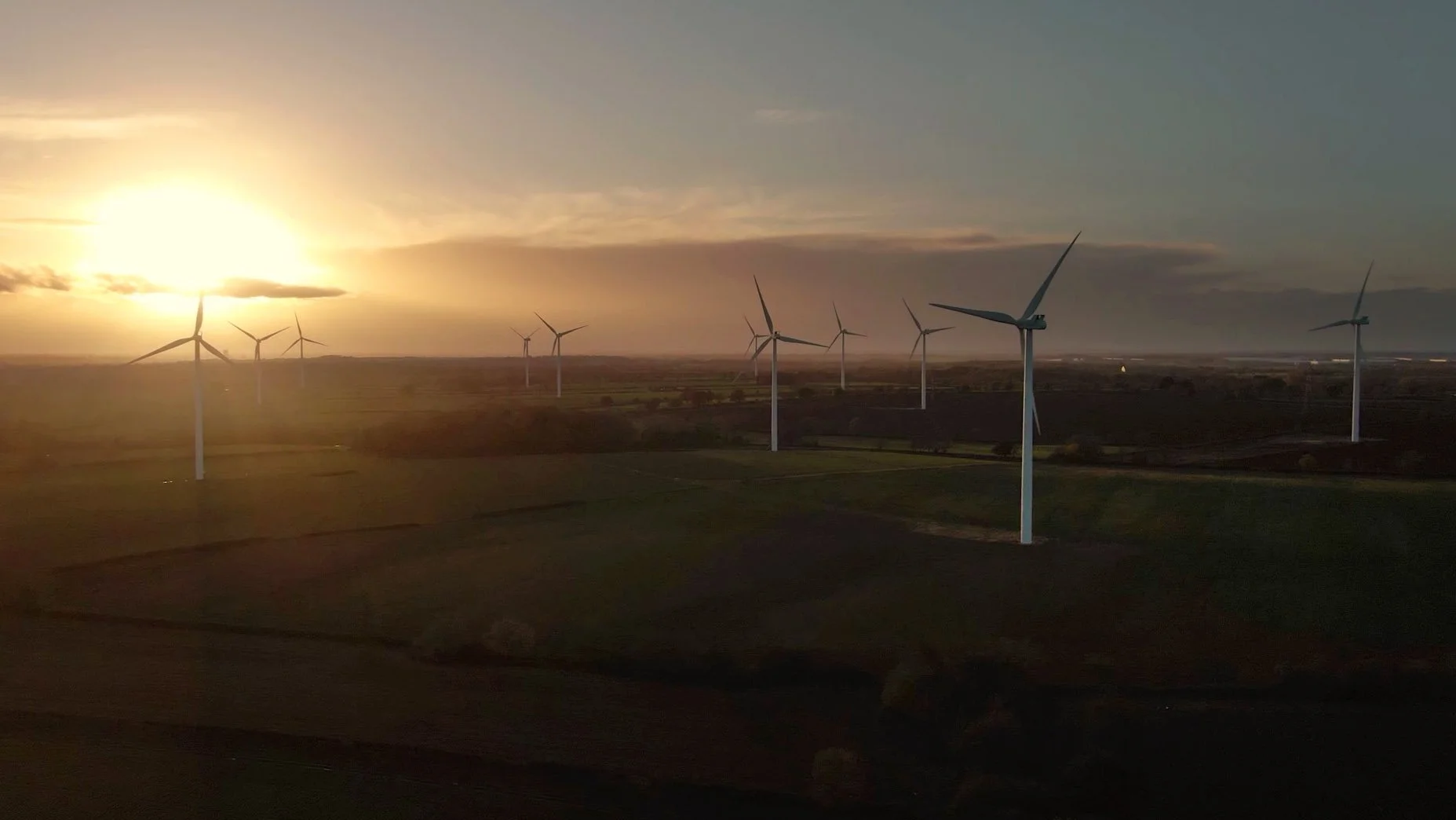 Aerial drone view of a wind farm, showing rows of wind turbines across the landscape and the scale of renewable energy infrastructure.