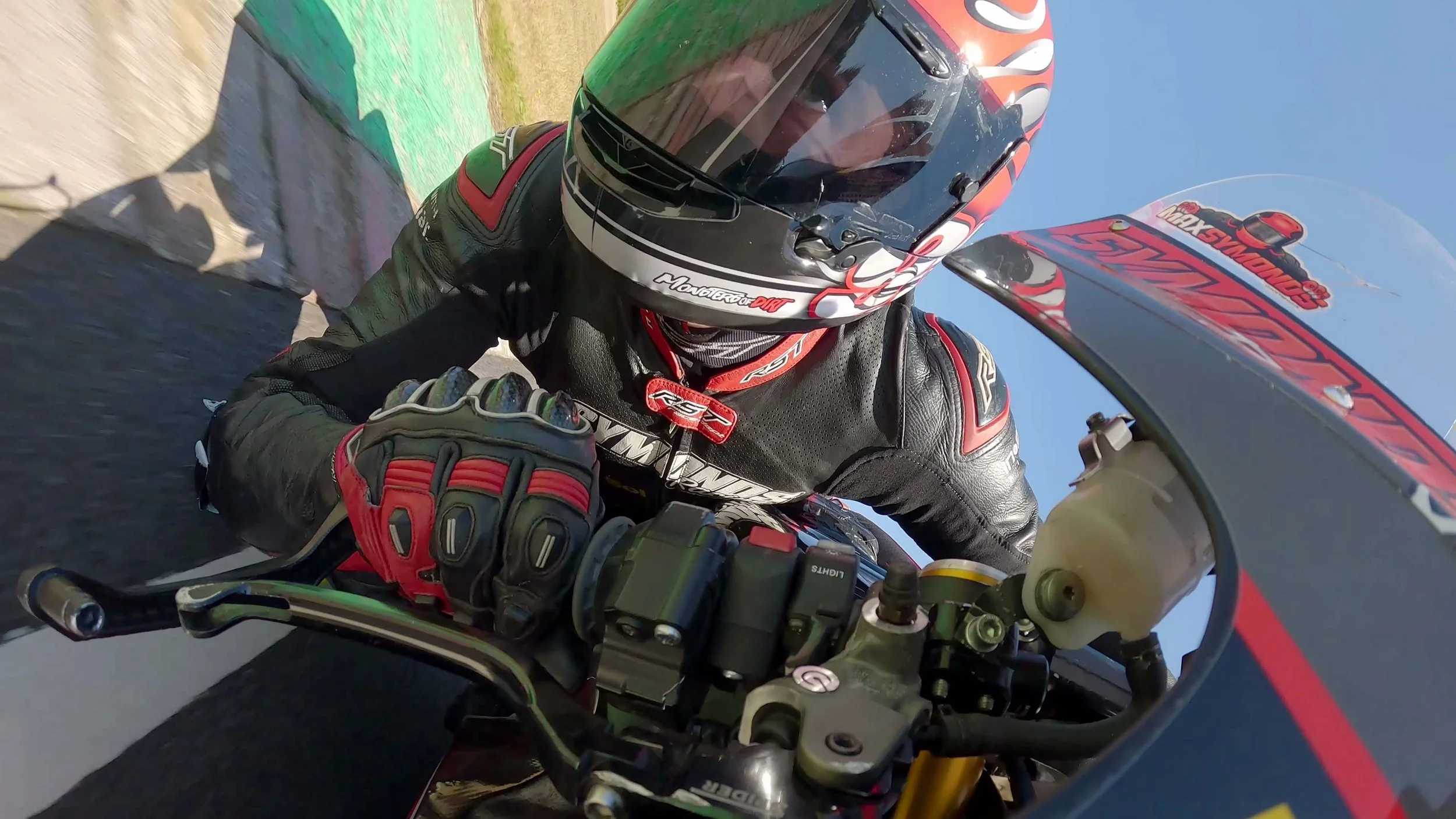 FPV drone view at Castle Combe Circuit, tracking a racing motorcycle at speed through the circuit with close-proximity motorsport action.