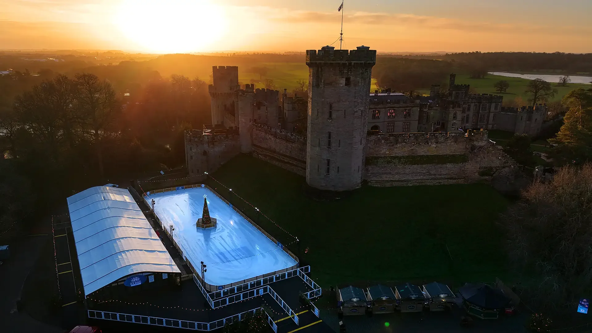 Lewis Whyld's drone view of an outdoor ice rink beside the historic Warwick castle at sunset.