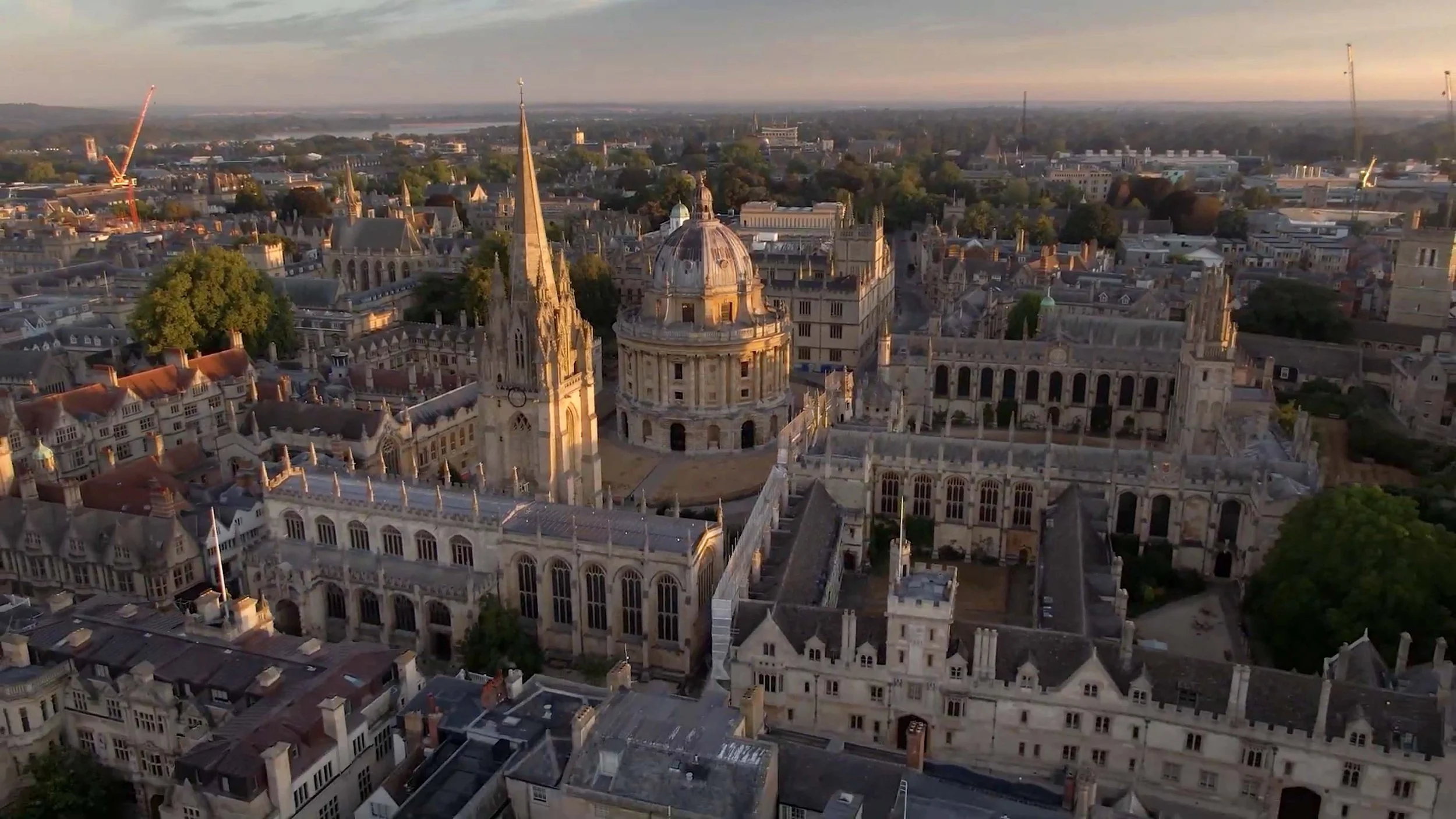 Aerial drone view of Oxford University at sunrise, showing the historic college rooftops, spires and distinctive architecture across central Oxford.