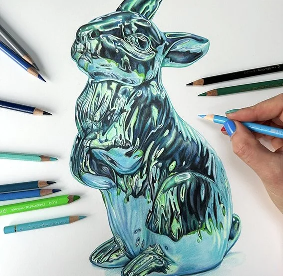 A hand drawing a colorful, abstract rabbit with professional pencils  surrounded by colored pencils on a white surface.
