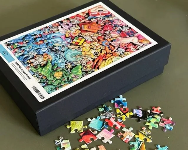 A jigsaw puzzle box with colorful artwork and several puzzle pieces scattered in front of it.