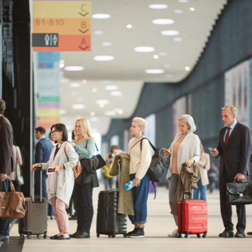 People in line with carry-on luggage at an airport terminal.