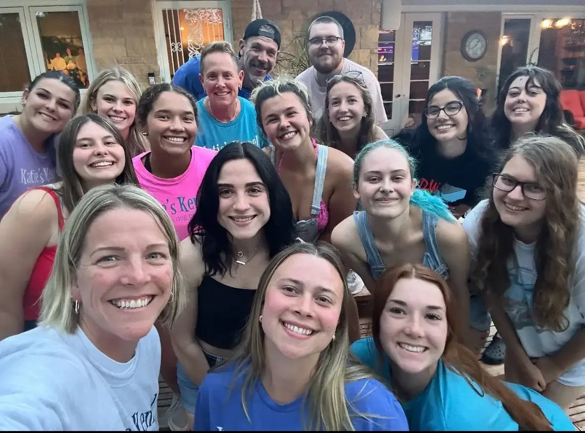 Group of young women and a few men smiling together at a social gathering indoors near a dog boarding facility in Omaha, NE