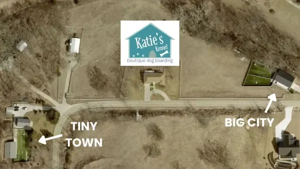 Aerial view of Katie's Kennel with labels indicating a tiny town to the left and a big city to the right, showing a rural area with houses, roads, and open fields at a dog boarding facility in Omaha, NE.