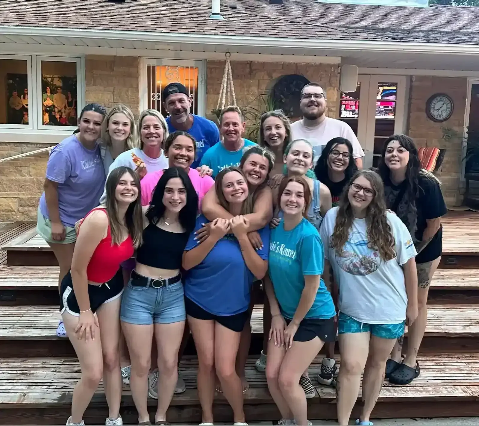 Group of 17 people smiling and posing on wooden steps outside a house near Katie’s Kennel in Omaha, NE
