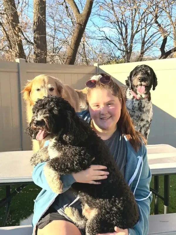 Smiling girl sitting on a bench with three dogs in a fenced yard at a dog boarding facility in Omaha.