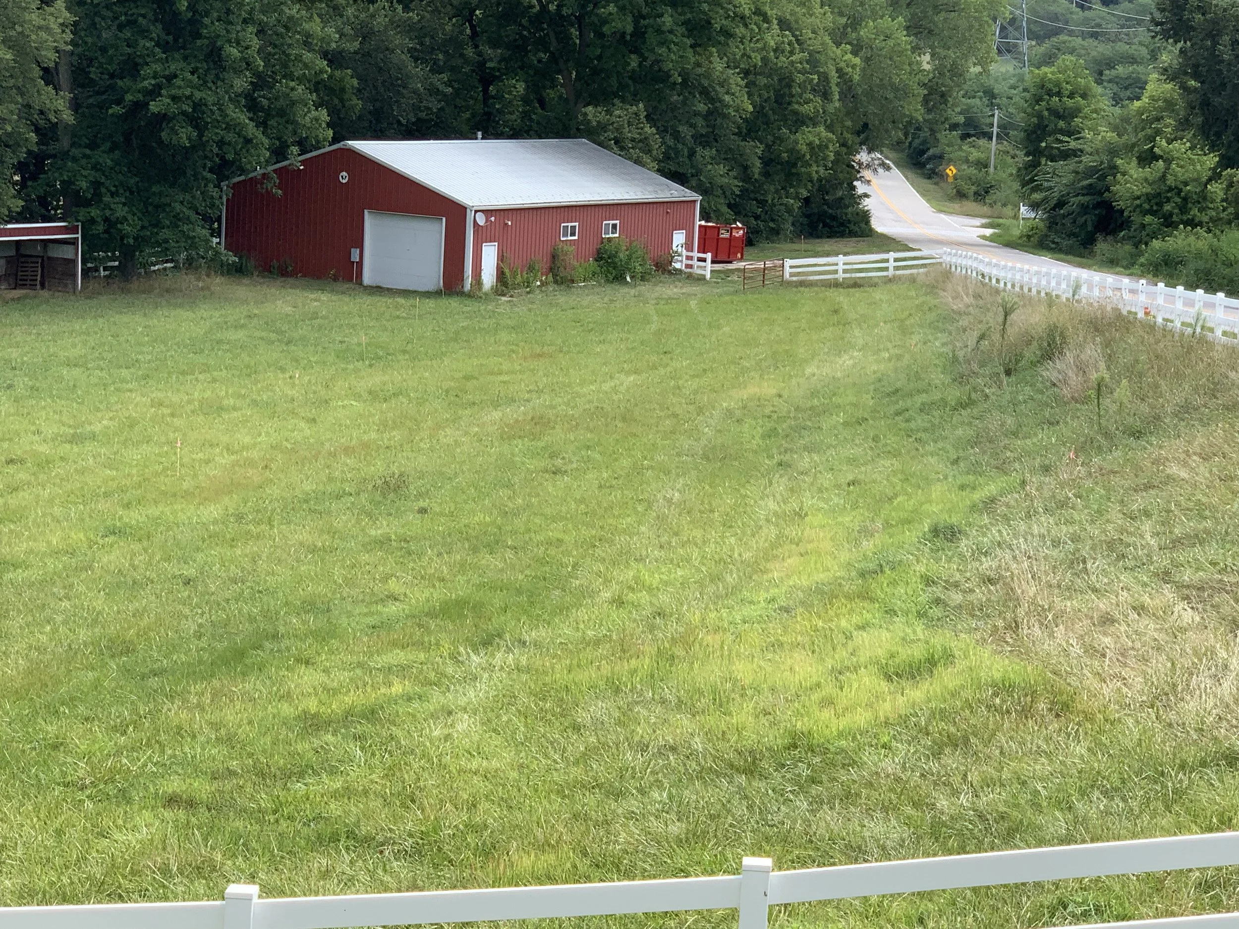 A rural scene with a red barn, a white fence, a grassy field, and a road with trees and power lines in the background near a dog boarding facility in Omaha, NE