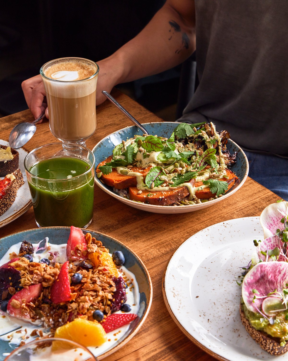  Breakfast diners enjoying a Sand Hill power bowl featuring maitake mushroom and garnet yam along with a Greek yogurt and fresh berry parfait, cold-pressed juice, and a latte. 