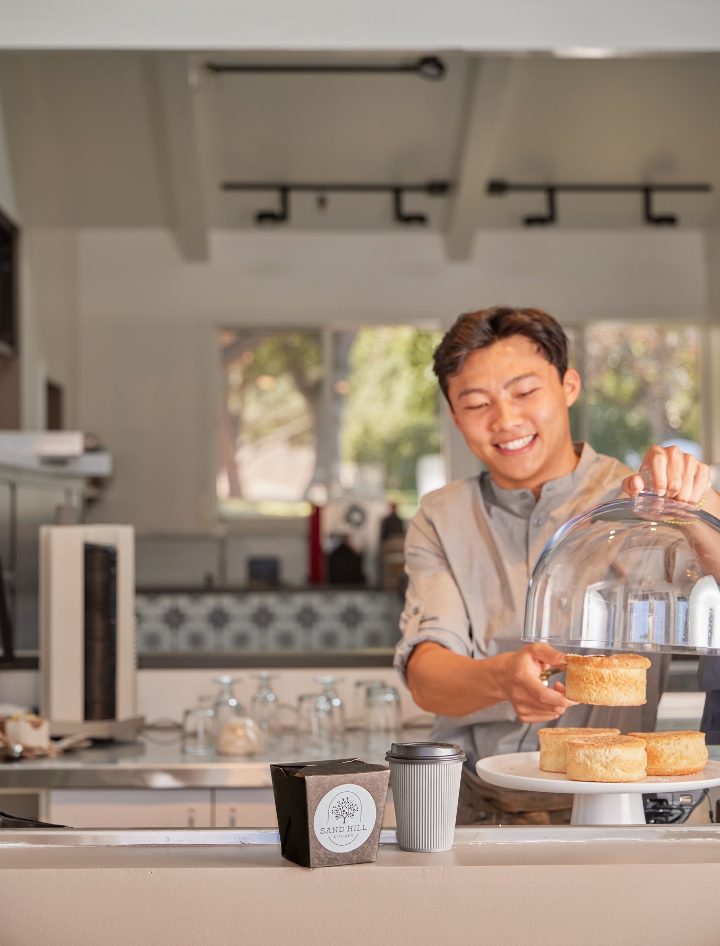  Smiling server taking a pastry out of a glass case for a to-go breakfast order. 