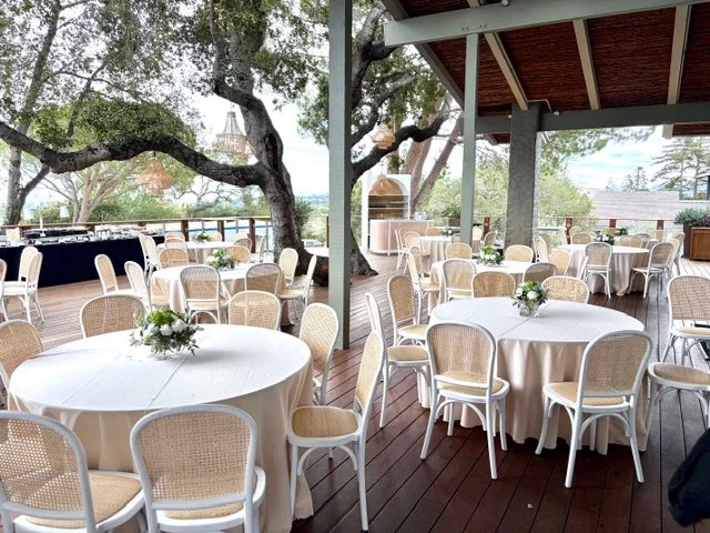 Outdoor wedding reception on the Tree Deck at The Quad Conference Center with round tables, white tablecloths, cane chairs, and floral table arrangements.