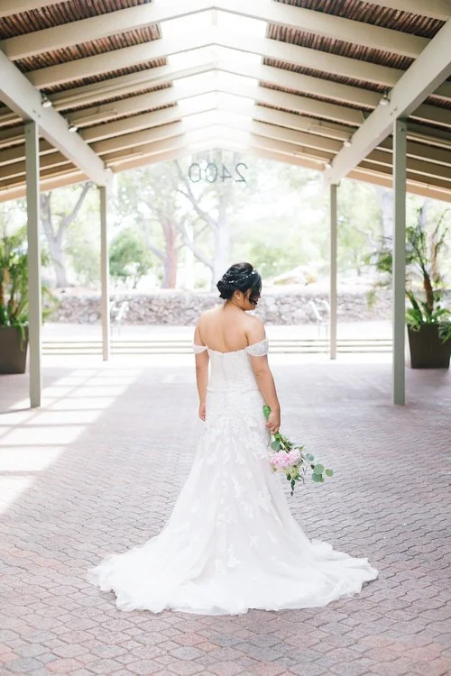 Bride in an off-shoulder white wedding dress holding a bouquet, standing under the covered walkway at The Quad Conference Center.