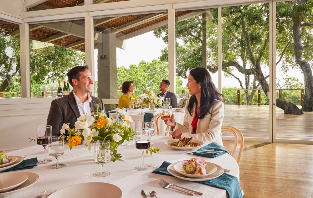 Two couples dining at an event at The Quad Conference Center sitting at white clothed tables with floral centerpieces, plated entrees, and glasses of wine.