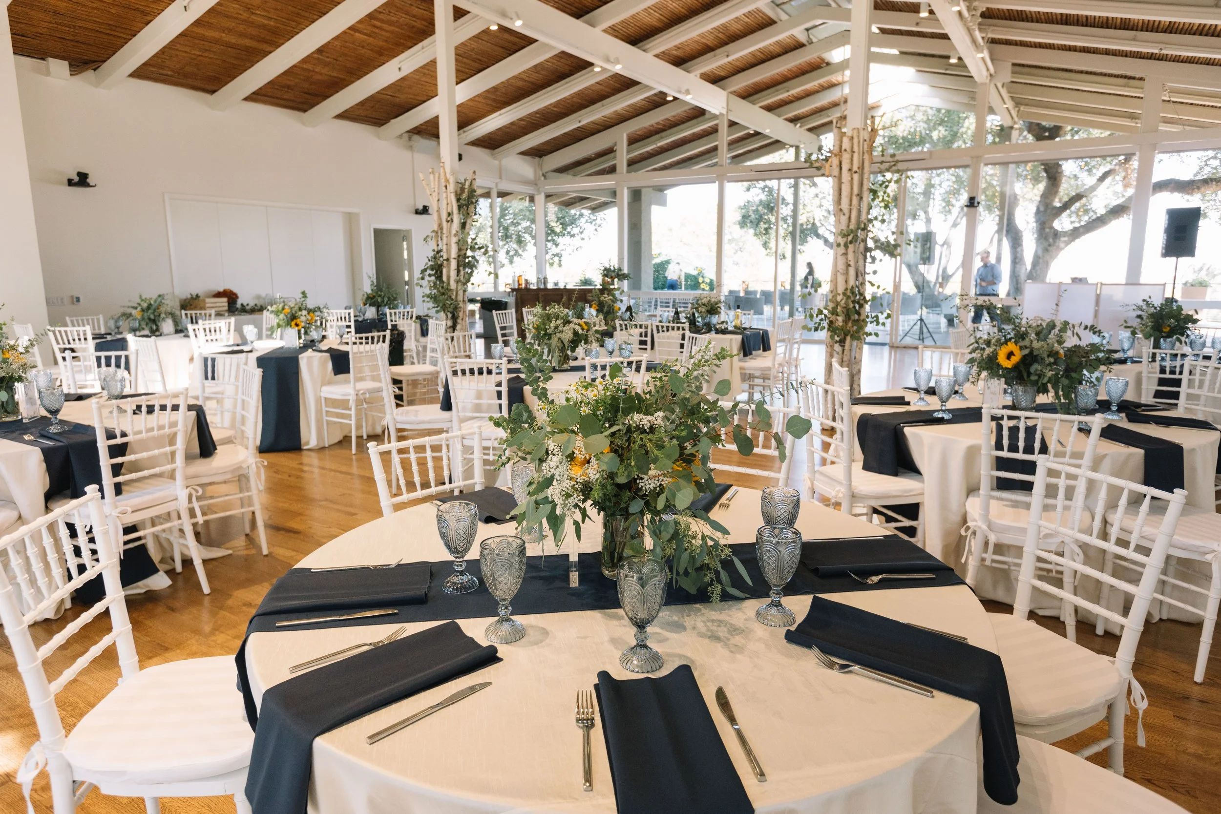 Elegant table setup for a wedding reception with white chairs, black napkins, decorative glasses, and sunflower centerpiece at The Quad Conference Center.