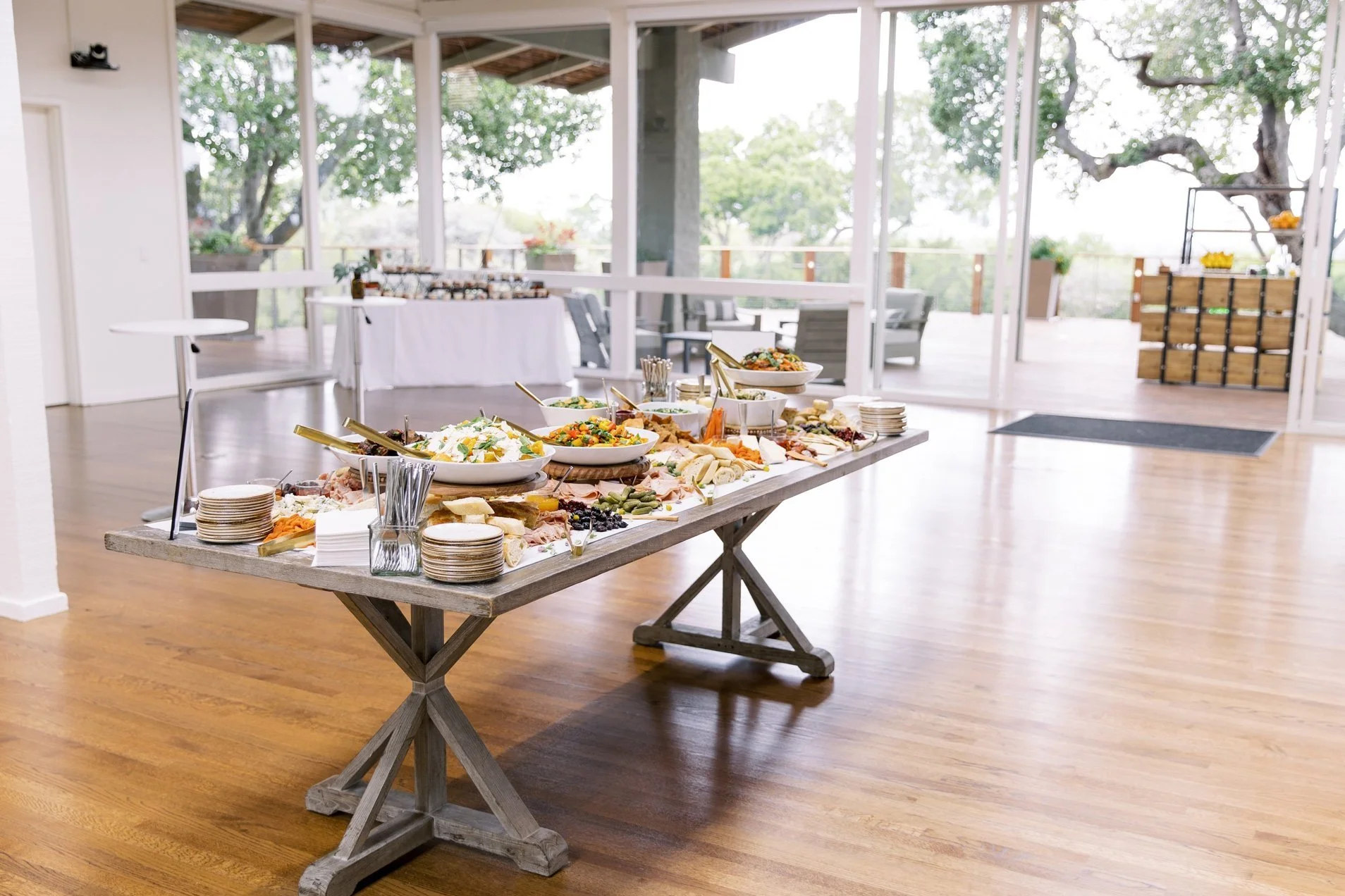 Long wooden table with assorted dishes and plates set for a buffet in the bright Quad Conference Center with large windows looking out onto the Tree Deck.