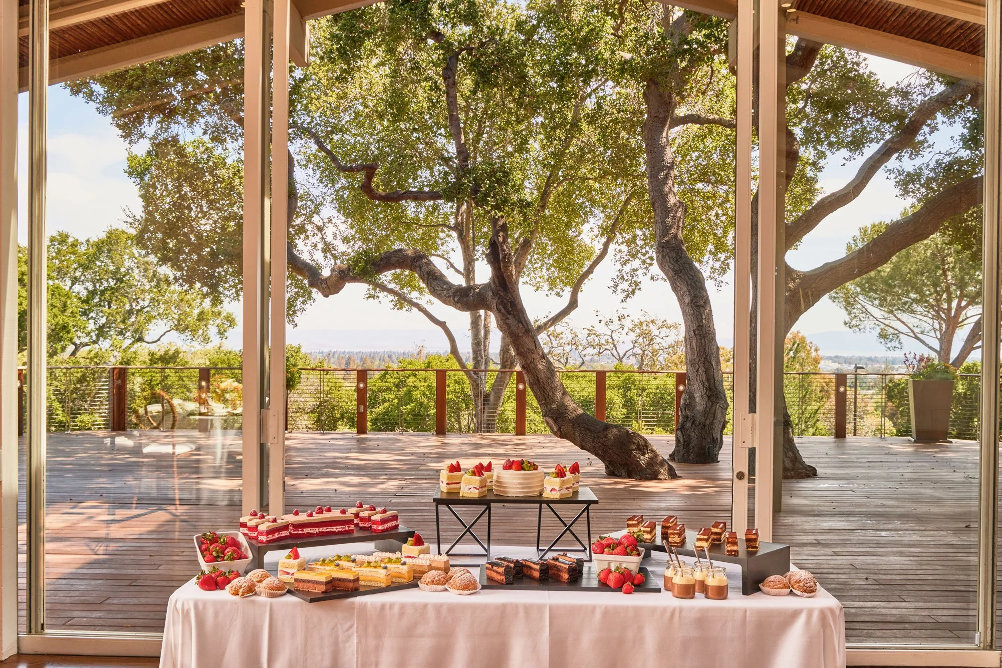Grazing table laden with assorted desserts and pastries in front of a picture window looking onto the Tree Deck at The Quad Conference Center.