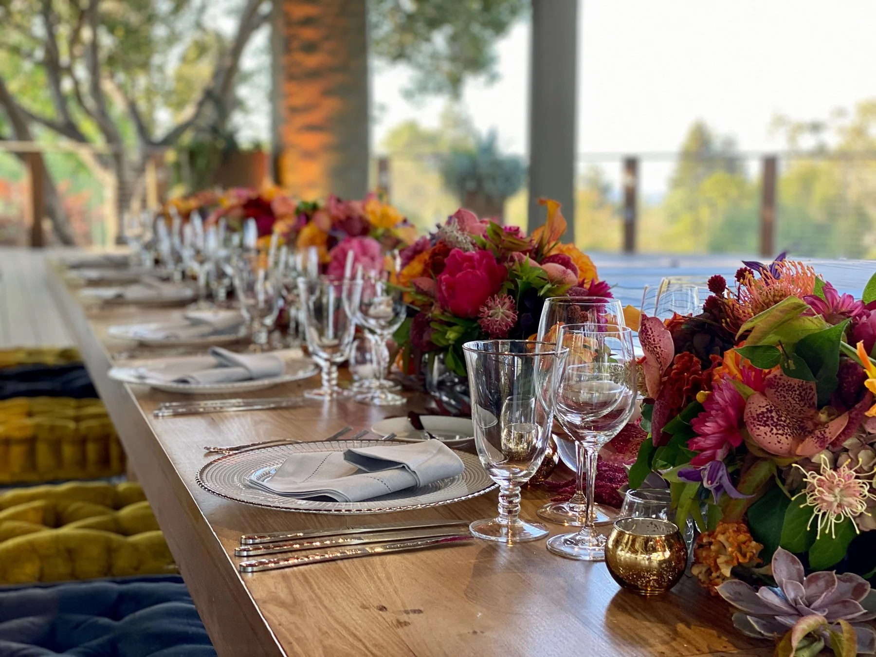 Elegant table setting with floral centerpieces, glassware, and napkins on a long wooden dining table at a wedding reception on the Tree Deck at The Quad Conference Center.