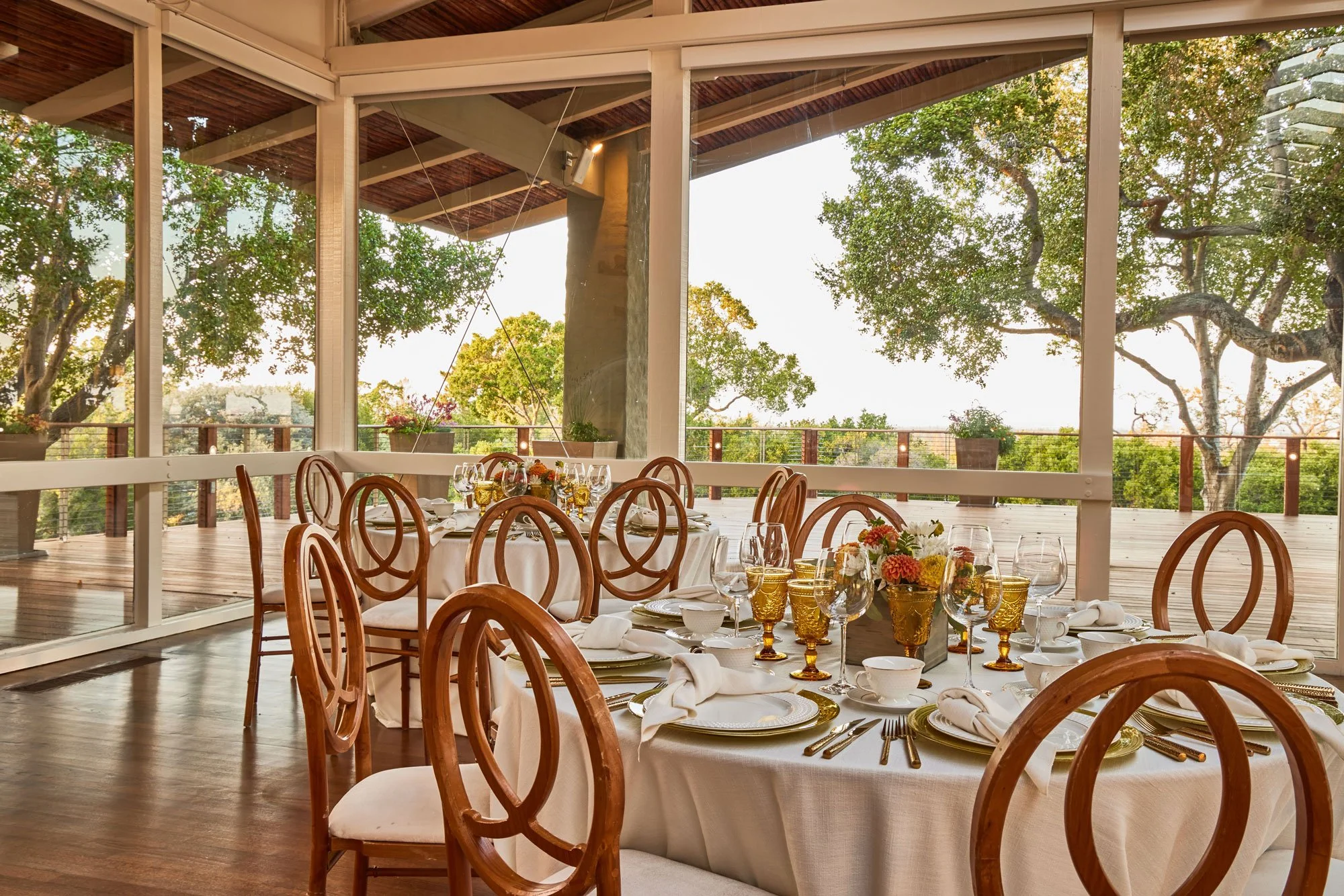 Elegantly set round tables await guests in front of picture windows that look out to the expansive Tree Deck at The Quad Conference Center.