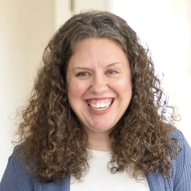 Smiling woman with curly brown hair in a casual setting.