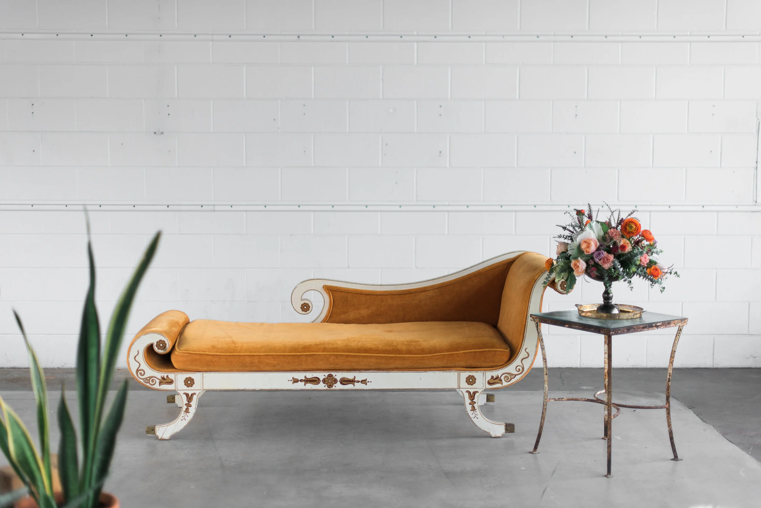 Copper vintage velvet fainting sofa styled on concrete floor with white wall and side table with florals