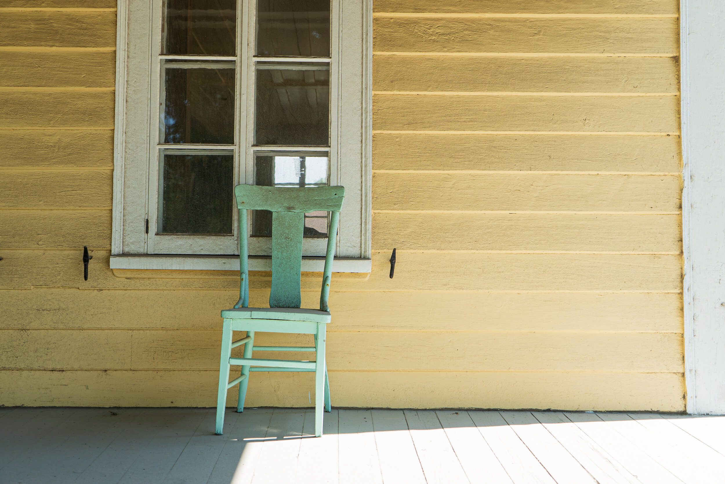 Green chair leaning against white window on yellow house | 2017